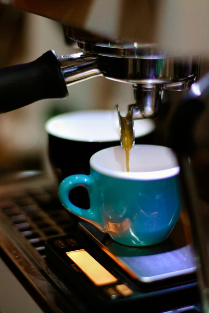 Close-up of coffee machine brewing espresso in a vibrant café setting, with cups and mugs ready.